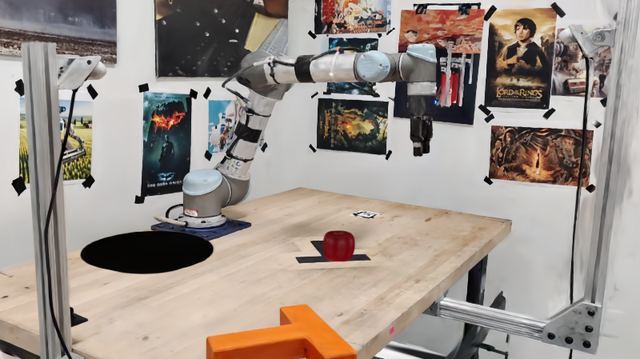 A photorealistic Gaussian-splat render of a UR5 robot arm reaching toward a red apple on a desk